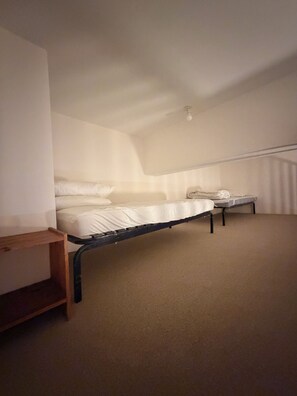 Une chambre avec un lit simple, une petite table et un plafond en pente.