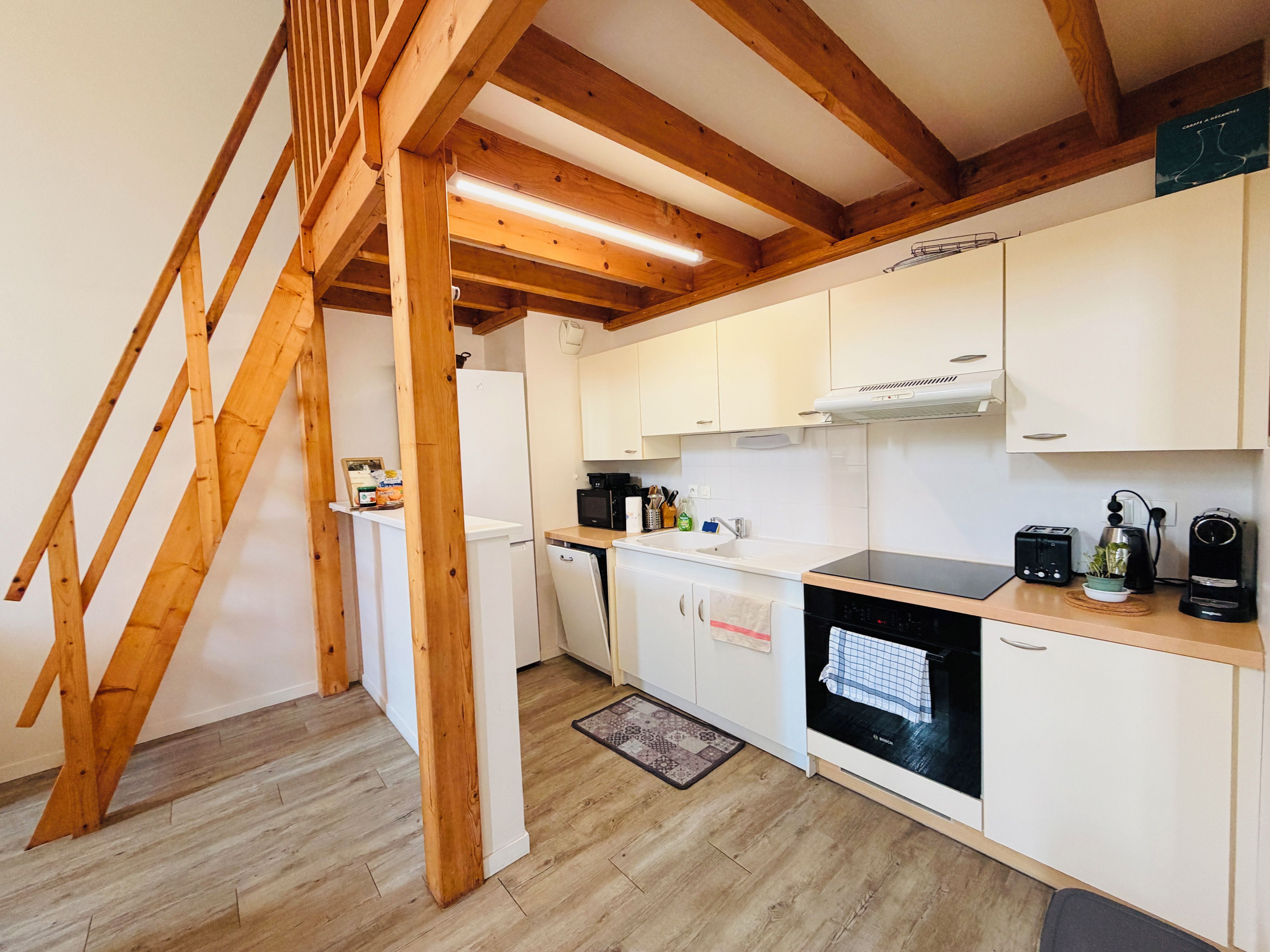 A kitchen with wooden beams, white cabinets, a black stove, and a wooden staircase.