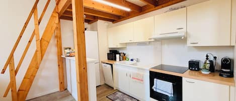 A kitchen with wooden beams, white cabinets, a black stove, and a wooden staircase.