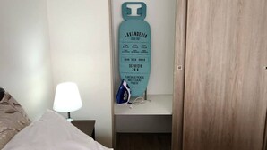 A hotel room with a bed, a nightstand with a lamp, a closet with a wooden door, and a sign indicating amenities like a minibar and a 24-hour service. - Acogedor Loft Centro De Santiago (Santiago)