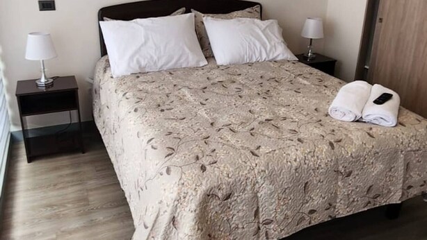A neatly made bed with a patterned bedspread, two bedside lamps, and a wooden floor. - Acogedor Loft Centro De Santiago (Santiago)