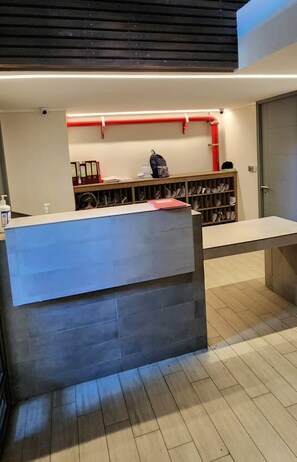 A reception desk with a counter, a shelf with shoes, and a red pipe on the wall. - Acogedor Loft Centro De Santiago (Santiago)
