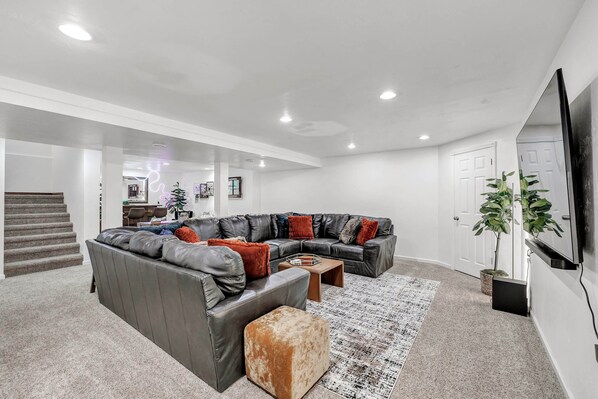 A modern living room with a sectional sofa, ottoman, coffee table, and a large flat-screen TV.