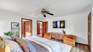 Ein Schlafzimmer mit einem großen Bett, zwei Sesseln, einem Fernseher und einem Deckenventilator.