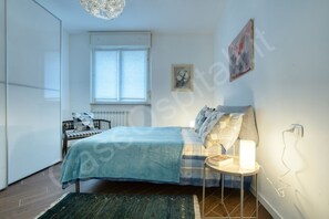 A bedroom with a bed, bedside table, lamp, and a window.