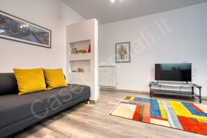 A modern living room with a grey sofa, yellow cushions, a flat-screen TV, a radiator, and a colorful rug.