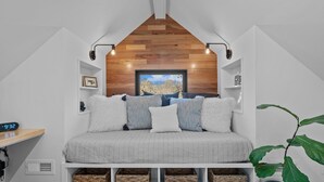 Una camera da letto accogliente con soffitto a falde, un letto con lenzuola a righe, un quadro incorniciato sopra il letto e una sveglia digitale sul comodino.