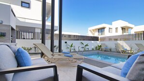 Un espace piscine extérieur moderne, doté de chaises longues et surplombant un ciel d’un bleu limpide.