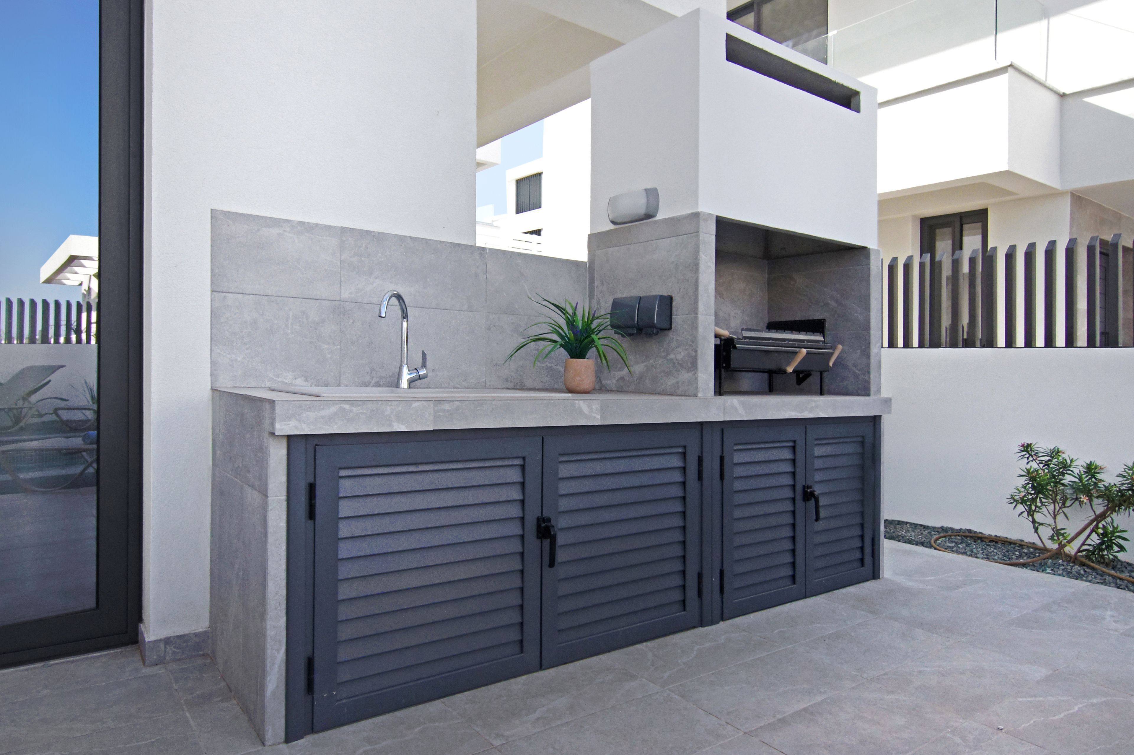 A modern outdoor kitchen area with a built-in sink, a potted plant, and a barbecue grill.