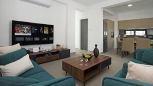 Un salon moderne avec un téléviseur à écran plat, une table basse avec des verres et des canapés de couleur turquoise.