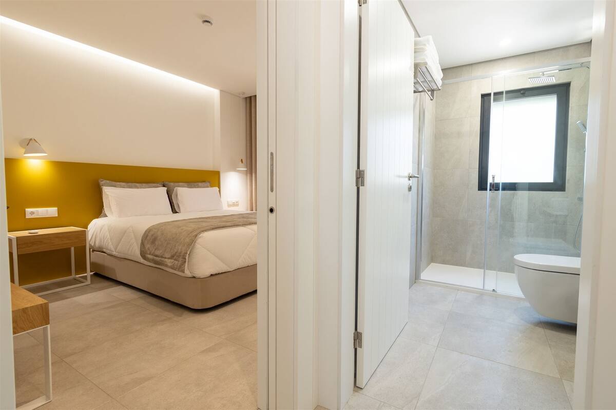 A modern bedroom with a bed, bedside table, and a bathroom with a shower and toilet.