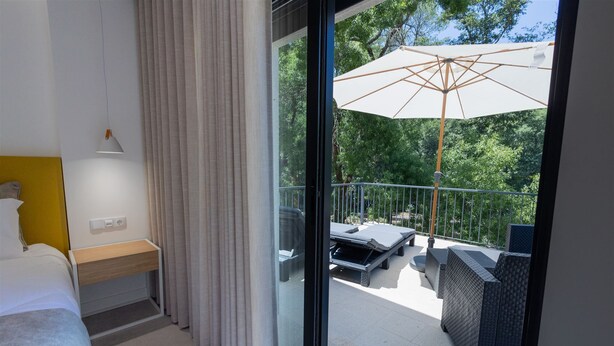 A hotel room with a bed, a bedside table, a window with curtains, and a balcony with outdoor furniture. - Be Alva (Oliveira do Hospital)