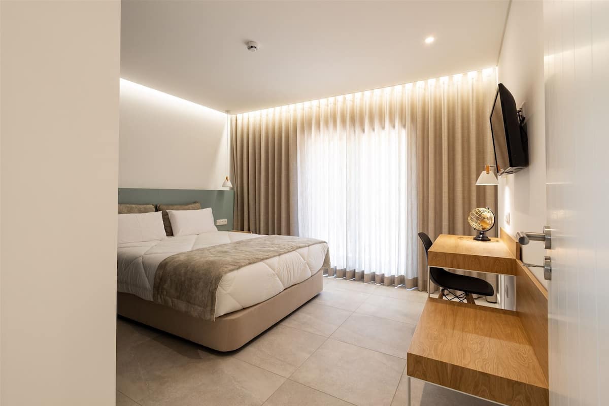 A modern hotel room with a large bed, a desk with a globe, and a TV mounted on the wall.