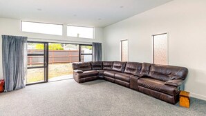 A spacious living room with a large sectional sofa, a sliding glass door leading to a backyard, and a carpeted floor. - Spacious, modern, centrally located house. (Geraldine)