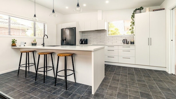 A modern kitchen with a central island, bar stools, white cabinetry, and a black refrigerator. - Spacious, modern, centrally located house. (Geraldine)