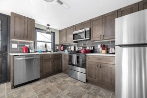 A modern kitchen with stainless steel appliances, dark wooden cabinets, and a tiled backsplash. - "Upper Magnolia": Renovated 2BR Apt off I-40, King Bed, 2 Queen + Kids Amenities (Statesville)