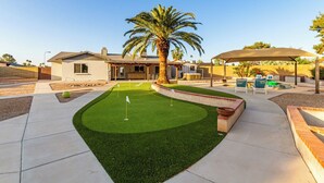 Una propiedad residencial con un césped cuidado, una palmera y un patio con mobiliario exterior.