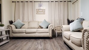 Una sala de estar con dos sofás color beige, un sillón de mimbre y piso de madera.