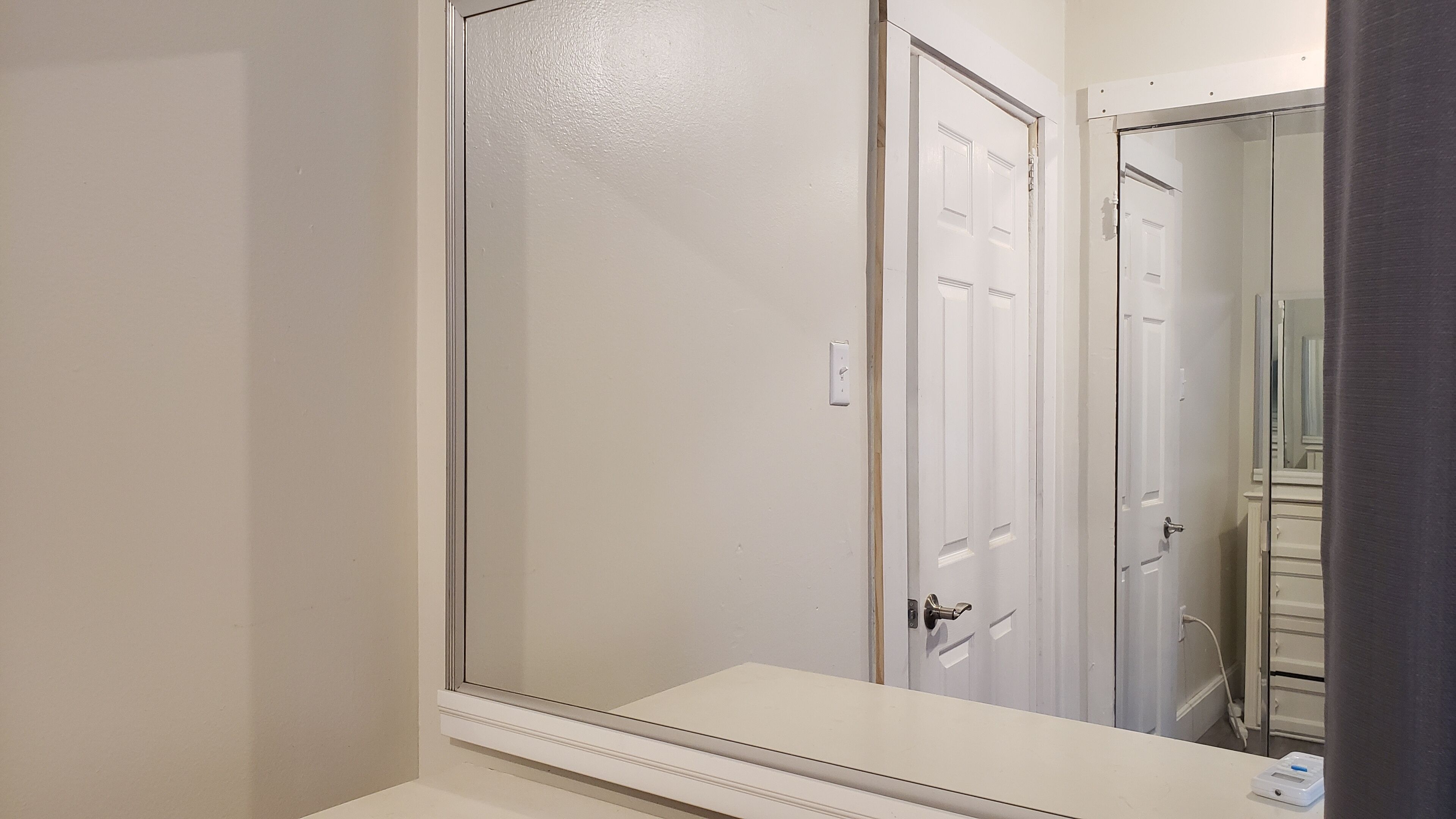 Une salle de bain avec un grand miroir, une porte blanche et un plan de toilette blanc.