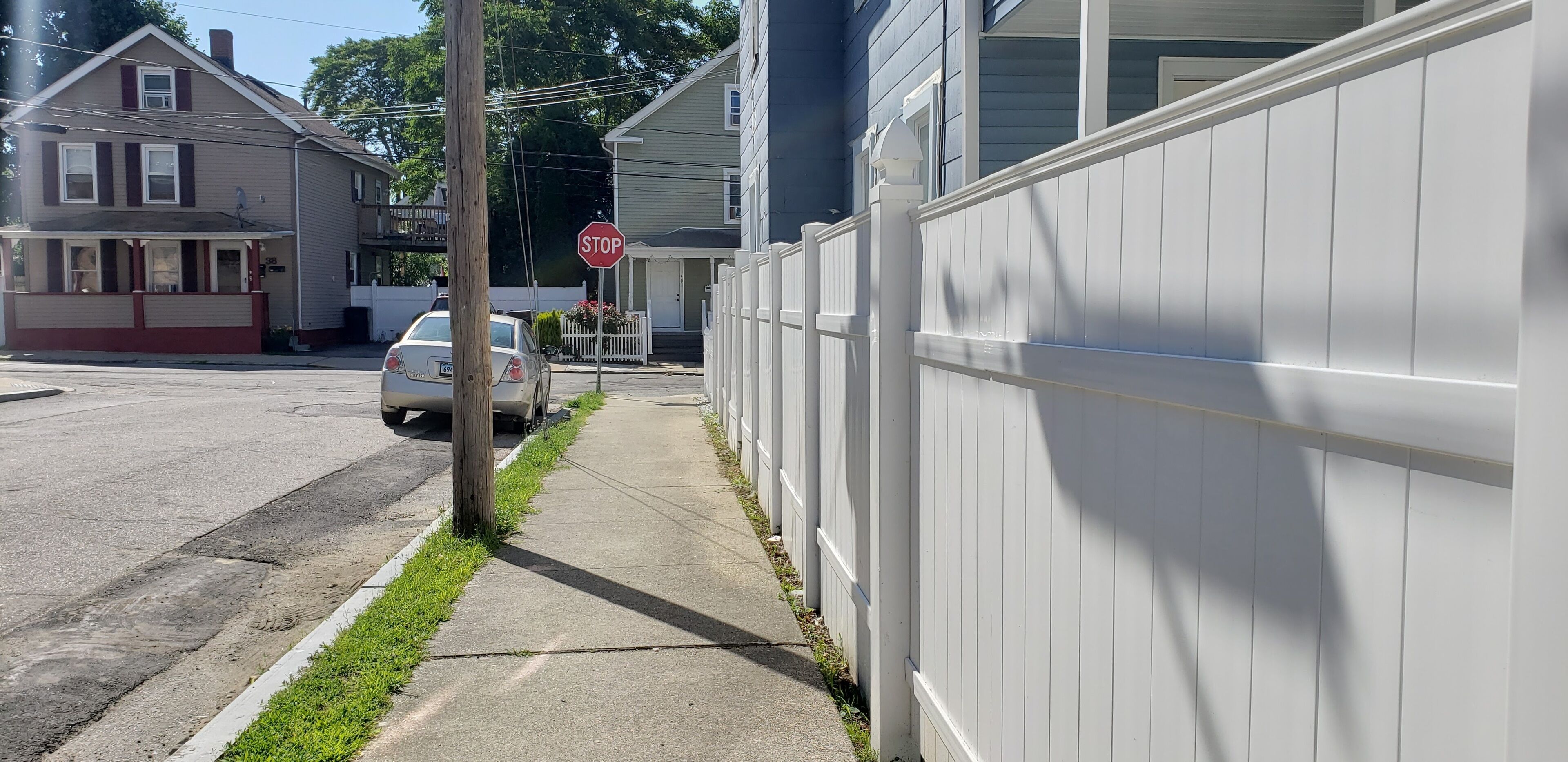 En boligvej med huse, et stopskilt og en parkeret bil langsiden.