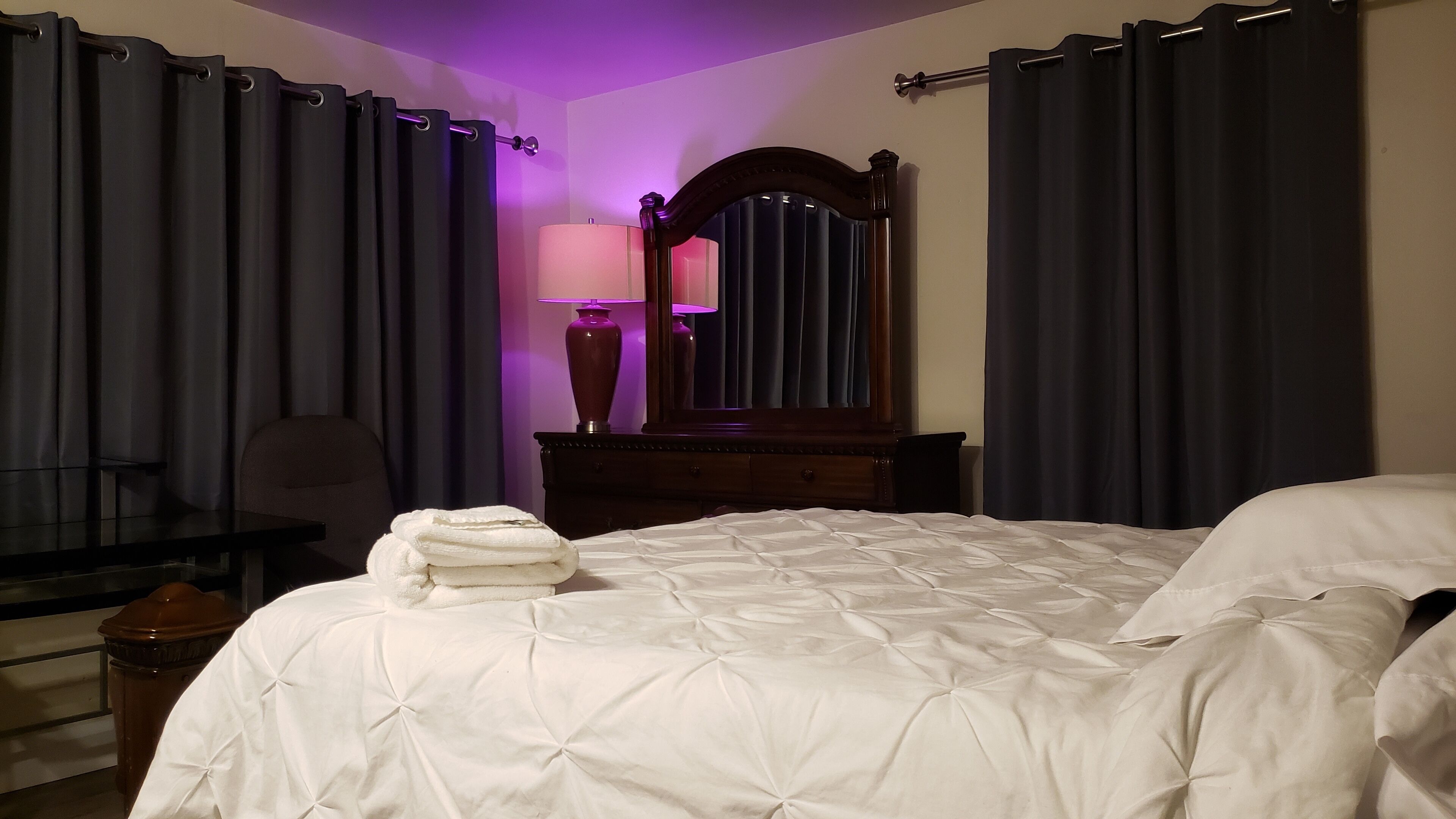 A hotel room with a bed, a desk, a chair, a mirror, and curtains.