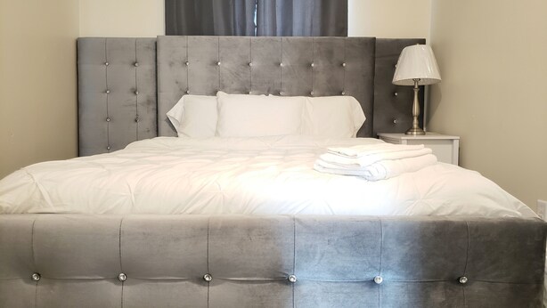 Una cama impecablemente tendida con un cabecero capitonado, ropa de cama blanca y una pila de toallas dobladas al lado.