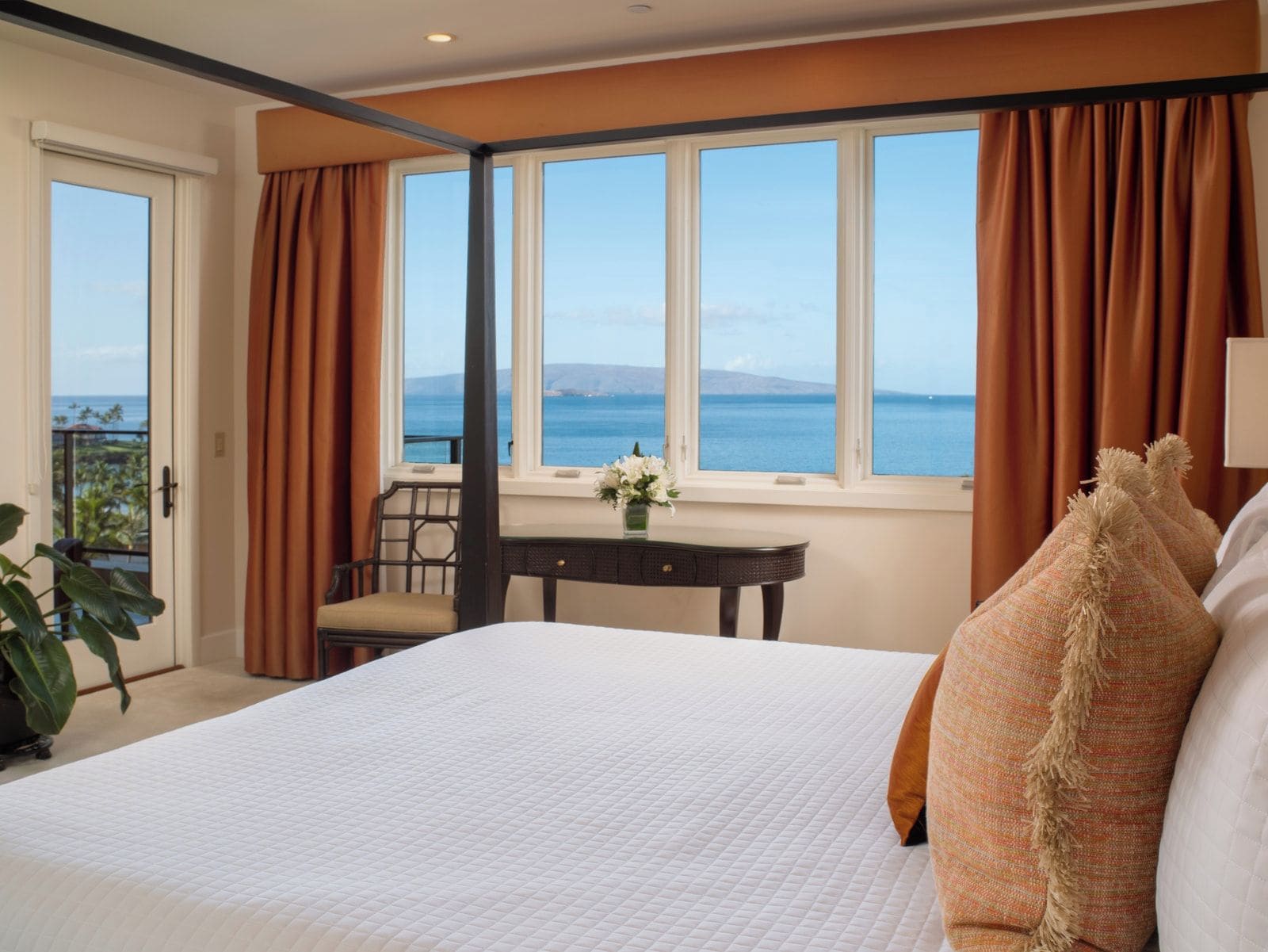 A hotel room with a large bed, a desk with a chair, a view of the sea, and a balcony.