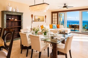A dining area with a glass table, white chairs, and a view of the ocean through large sliding doors. - Wailea Beach Villas Resort by KBM (Kihei)