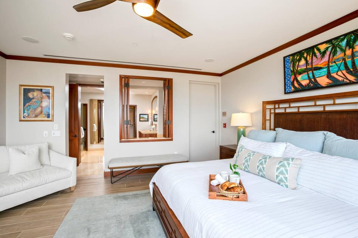 A hotel room with a bed, a sofa, a dining table, and a painting on the wall.