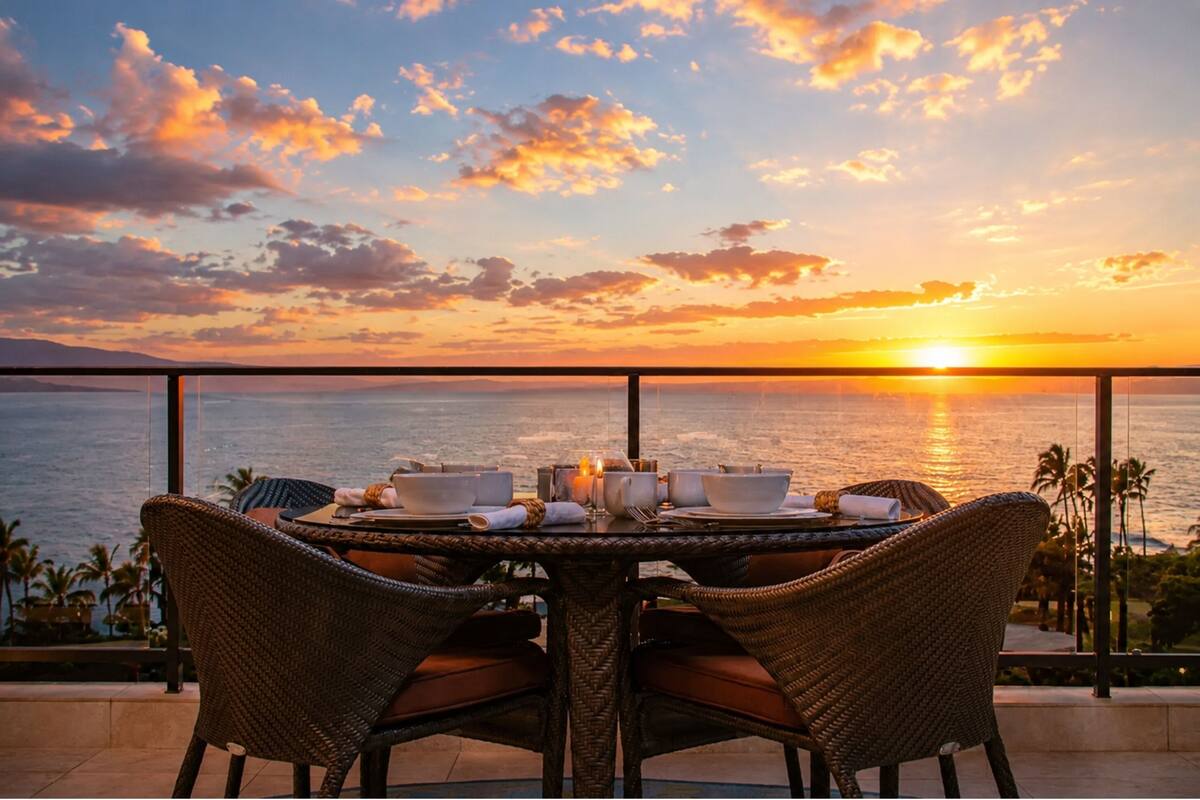 A table set for two with a view of the sunset over the ocean.
