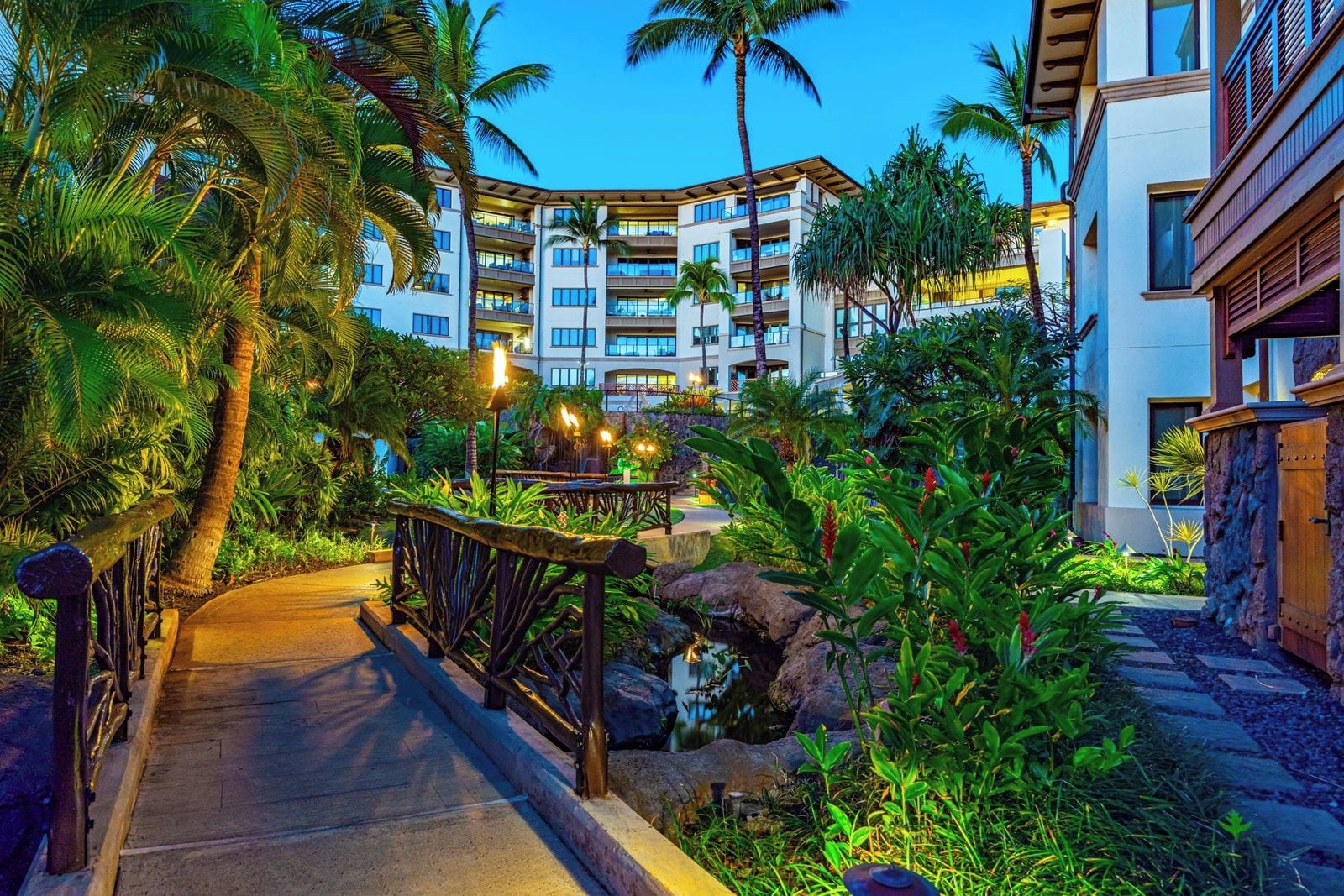 Un resort con un camino pavimentado, palmeras y un edificio con varios balcones.