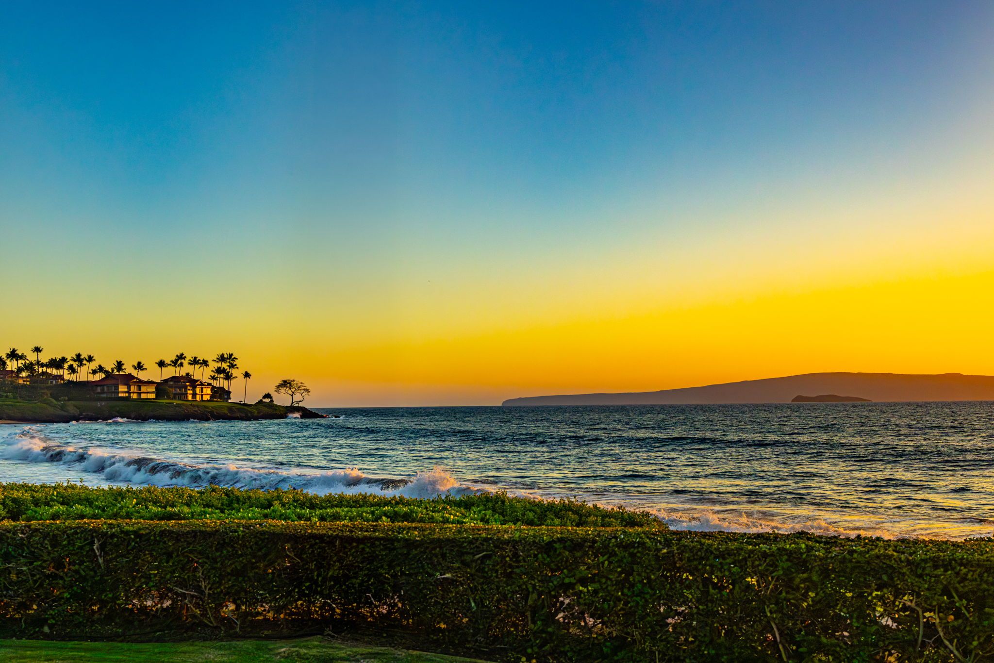 A coastal landscape with a clear sky, waves, and a distant landmass.