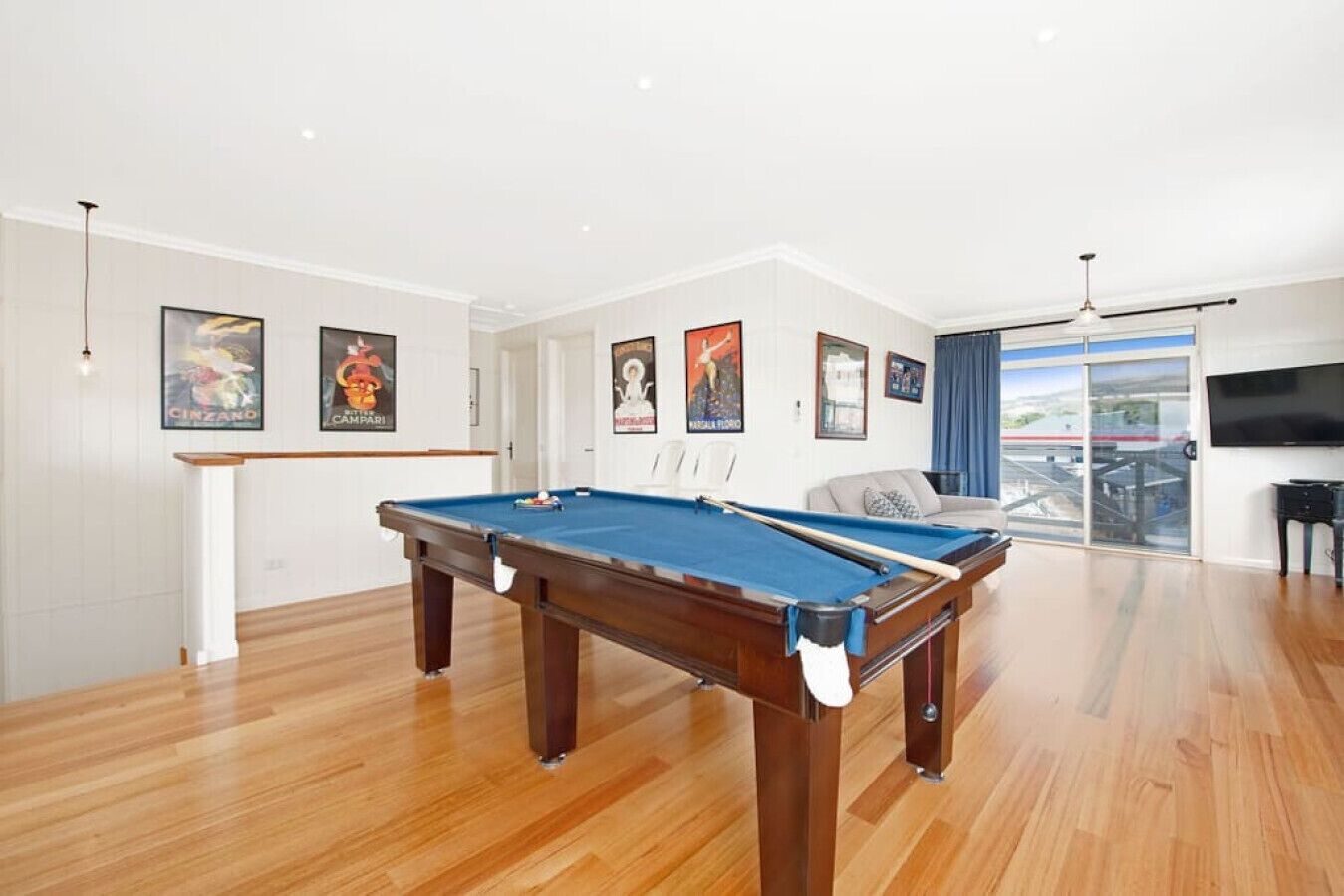 A pool table in a room with wooden flooring, white walls, and a large window with a view.