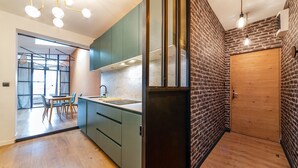 Une cuisine moderne avec un plan de travail en marbre, des armoires vertes et un mur d’accent en briques.