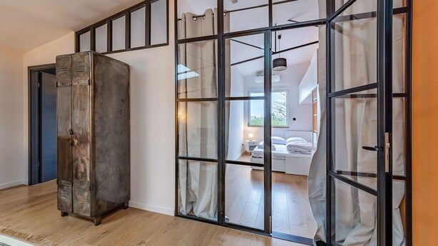 Un intérieur moderne avec une grande armoire, une cloison en verre et une chambre à coucher visible à travers cette cloison.