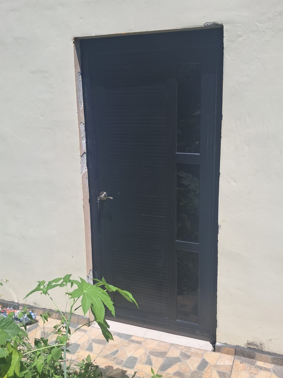 A closed door with a metal handle, set in a plain wall with a stone-tiled ground.