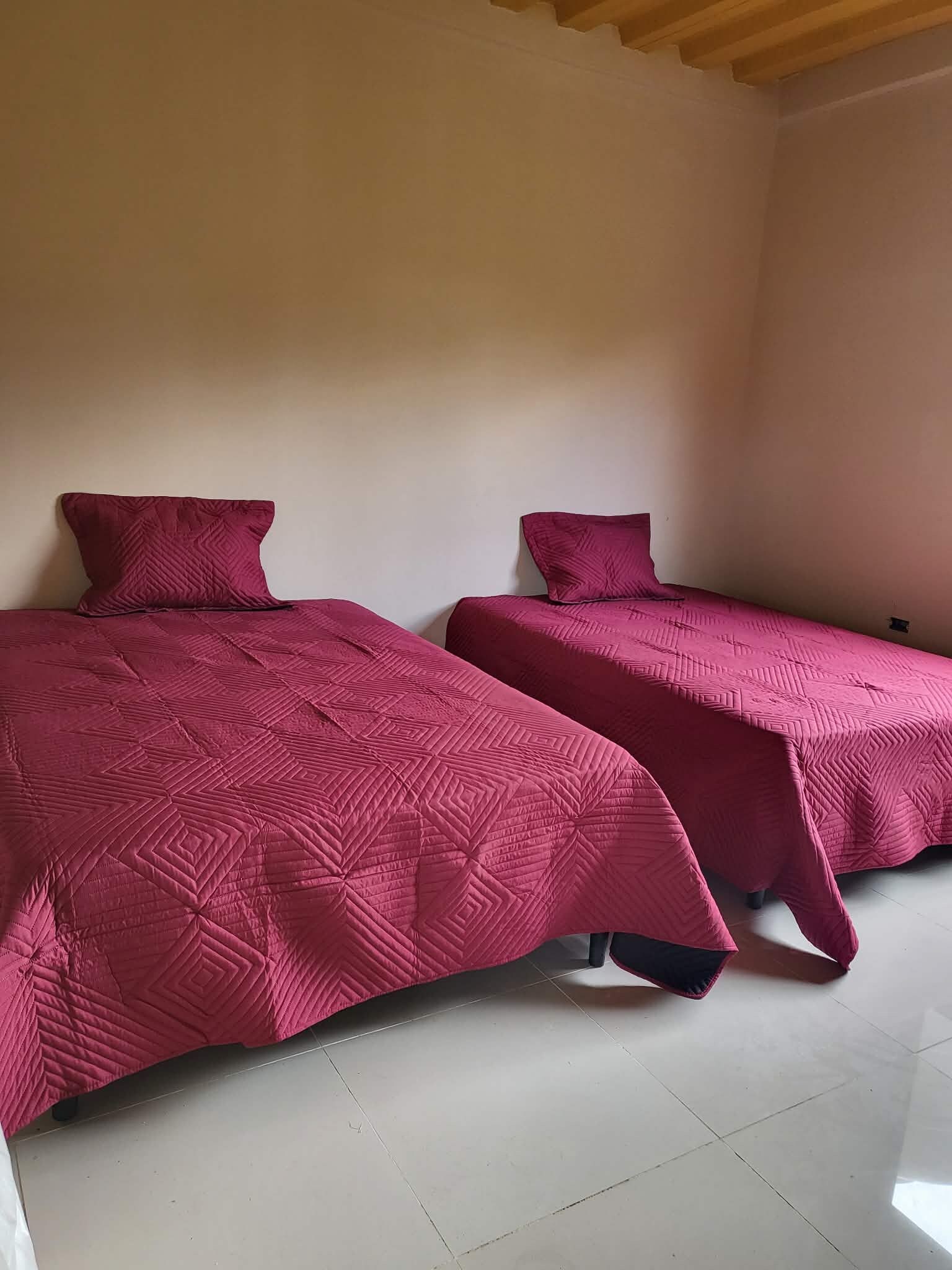 Dos camas individuales con cabeceras y pies de cama a juego, suelo de baldosas y techo de madera.
