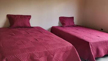 Dos camas individuales con cabeceras y pies de cama a juego, suelo de baldosas y techo de madera.