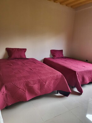 Twee eenpersoonsbedden met bijpassende hoofdborden en voetenborden, een betegelde vloer en een houten plafond.