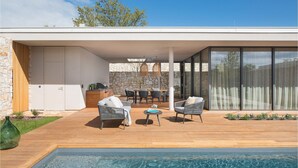 A modern outdoor living space with a pool, wooden deck, stone wall, and glass doors leading to an interior. - Beautiful home in Vodnjan with sauna (Vodnjan)