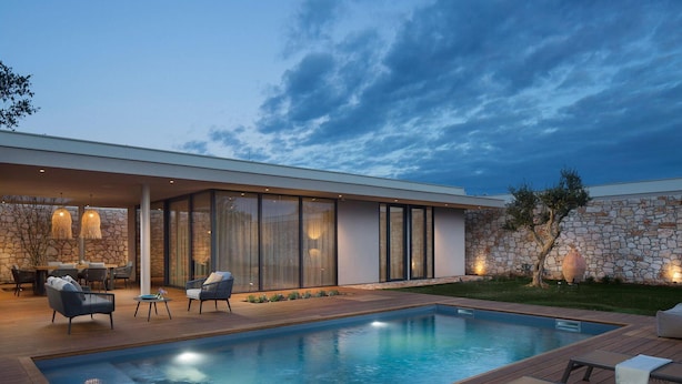 A modern outdoor pool area with a stone wall, lounge chairs, and a dining setup. - Beautiful home in Vodnjan with sauna (Vodnjan)