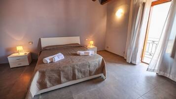 Une chambre à coucher avec un grand lit, deux tables de chevet avec des lampes, une fenêtre avec des rideaux et une vue sur le balcon.