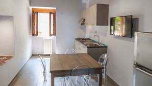 A modern kitchen with a wooden table and chairs, a built-in stove, and a TV mounted on the wall.