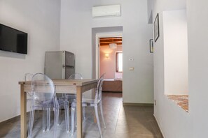 A modern kitchen with a wooden table and clear chairs, a refrigerator, and a flat-screen TV mounted on the wall.
