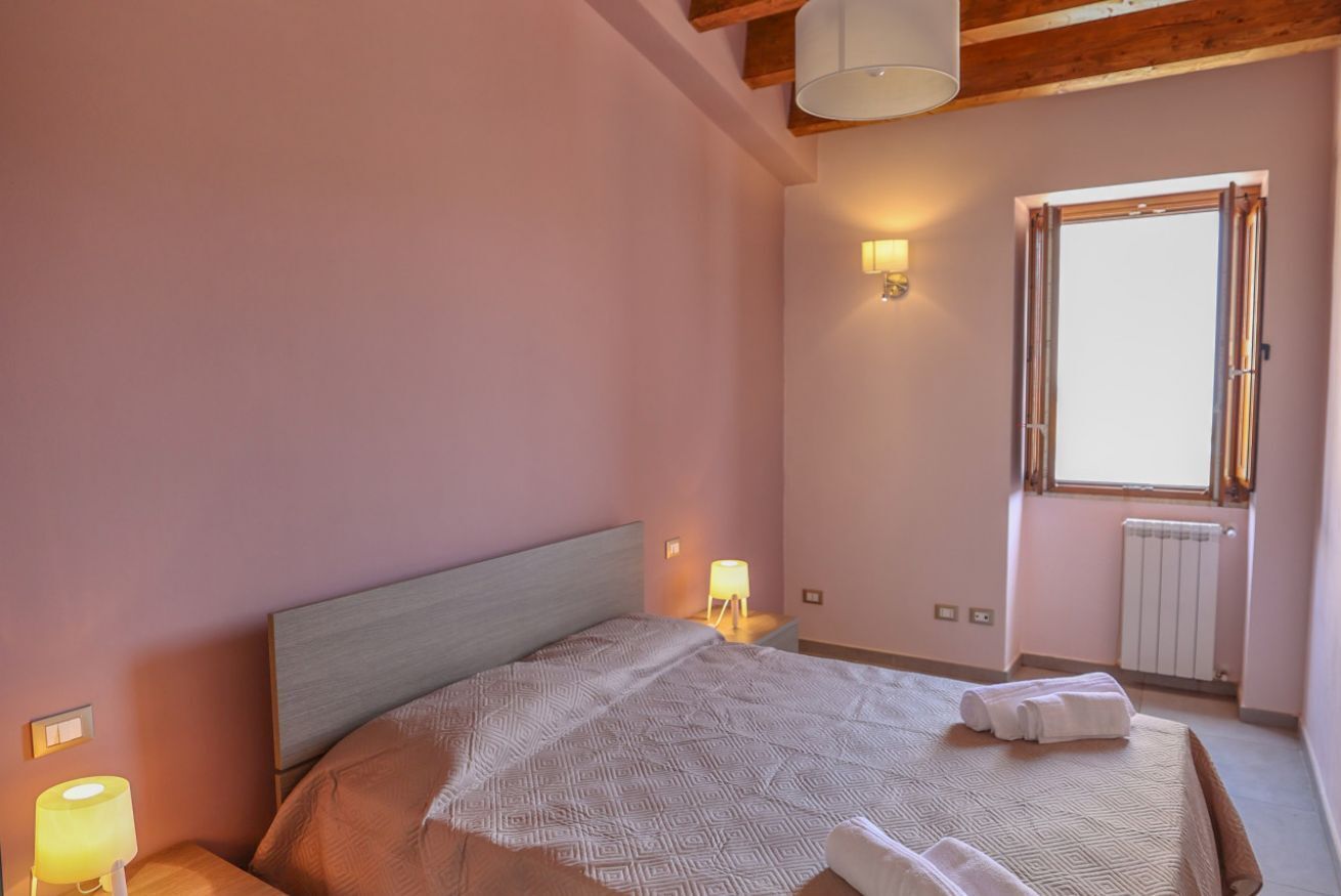 Una camera da letto con un letto, lampade sui comodini, una finestra e un termosifone.