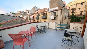 Terraza en la azotea con mobiliario exterior, incluyendo sillas y mesas de metal rojo y negro, y vistas de los edificios circundantes.
