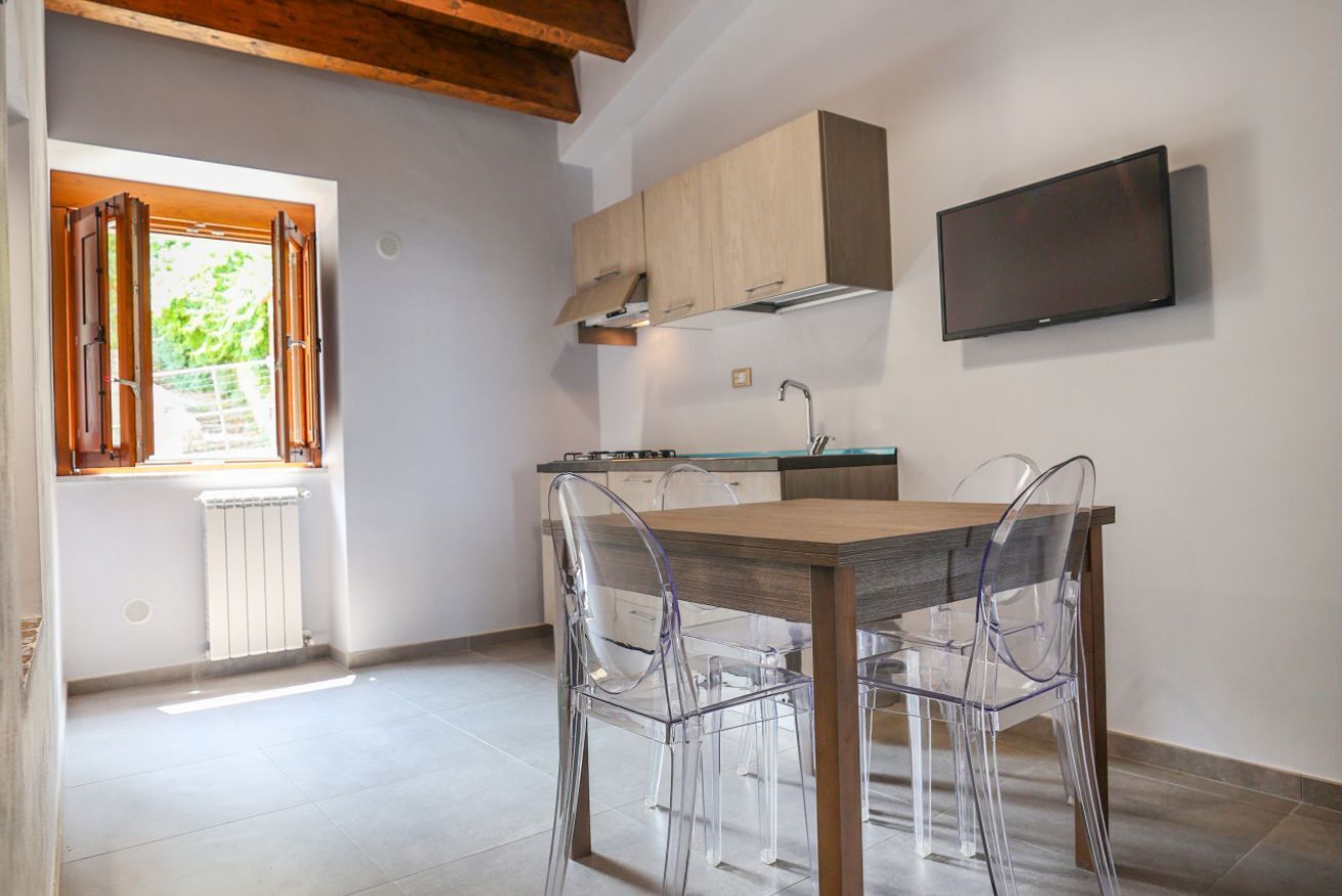 Eine moderne Küche mit einem Holztisch, klaren Stühlen, einem eingebauten Ofen und einem an der Wand montierten Fernseher.