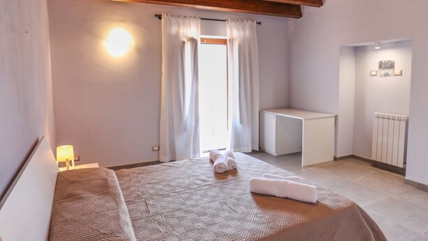 A bedroom with a bed, a desk, a radiator, and a window with curtains.