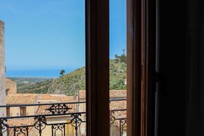 A balcony with a view of a coastal landscape, including terraced buildings and a hill.