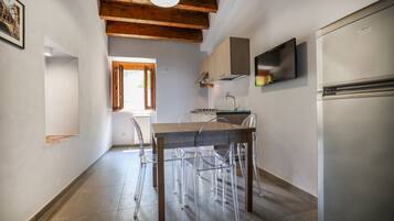 A kitchen with a wooden ceiling, a built-in oven, a refrigerator, and a window with wooden shutters.
